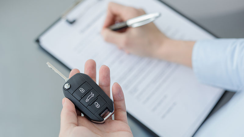 mão esquerda segura chave de rent a car enquanto a direita preenche contrato